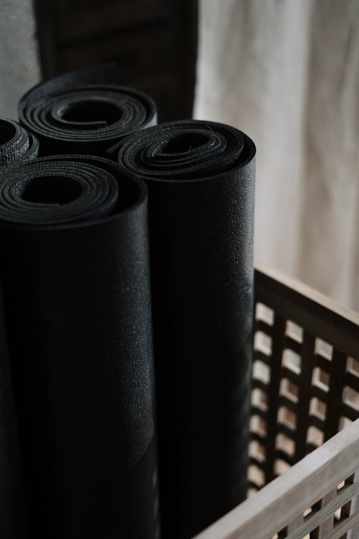 Usługi Close-up view of black yoga mats rolled and stacked in a wooden basket indoors.
