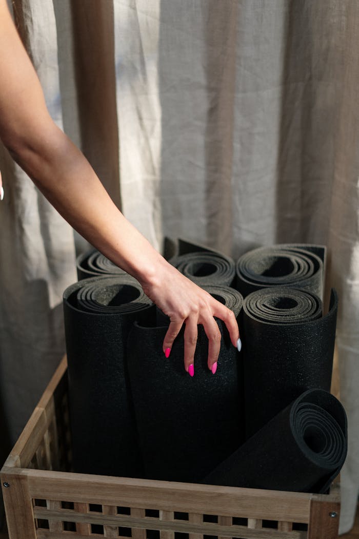 O Nas Close-up of a hand selecting a yoga mat from a basket in a yoga studio.